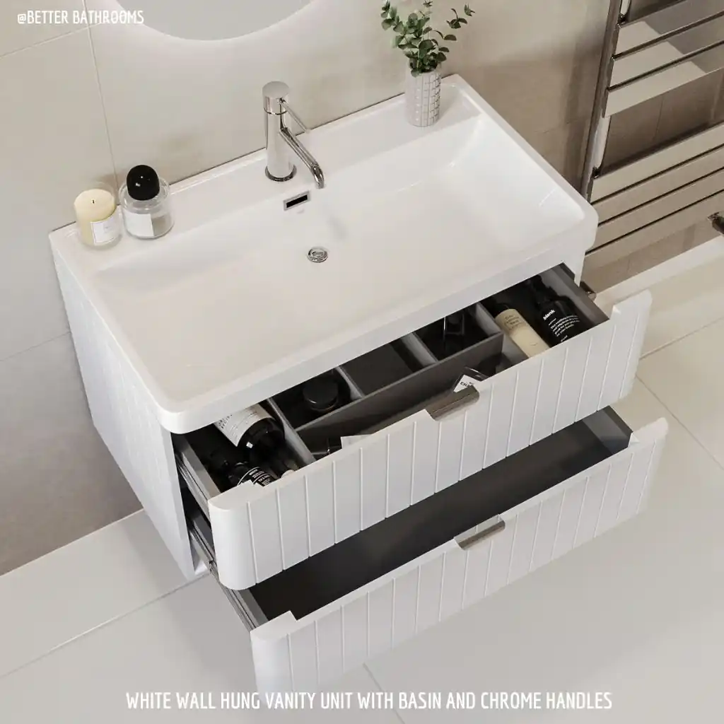 A white wall-hung bathroom vanity unit with a basin and chrome handles, featuring two open drawers filled with toiletries in a modern, small bathroom design setting.