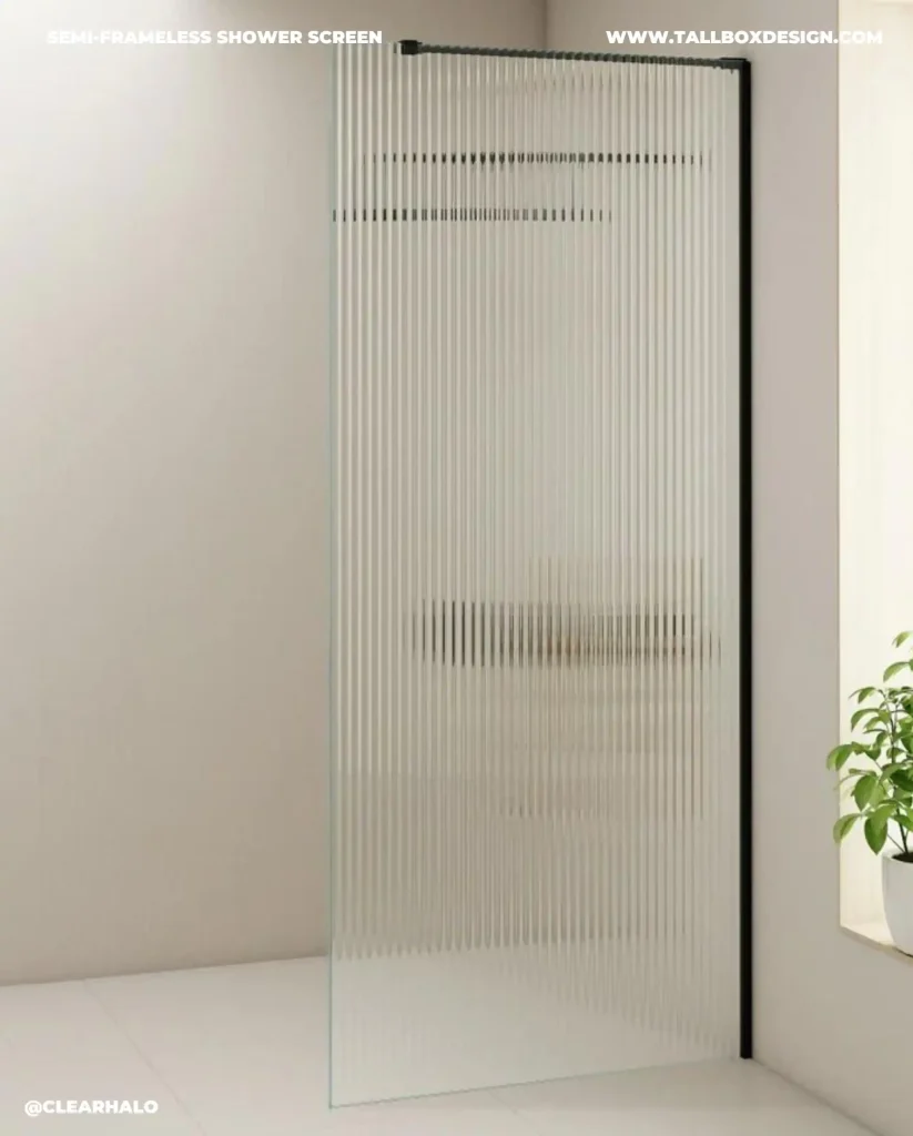 A vertical fluted glass fixed shower screen in a modern bathroom with a small plant in the corner. Text on the glass reads "Semi-Frameless Shower Screen," "ClearHalo," and "tallboxdesign.mom.